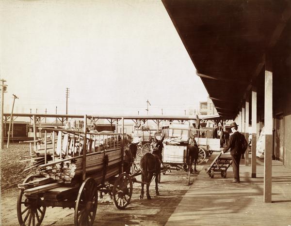 Wagons loaded with wood along a loading dock outside an agency or factory of the McCormick Harvesting Machine Company.