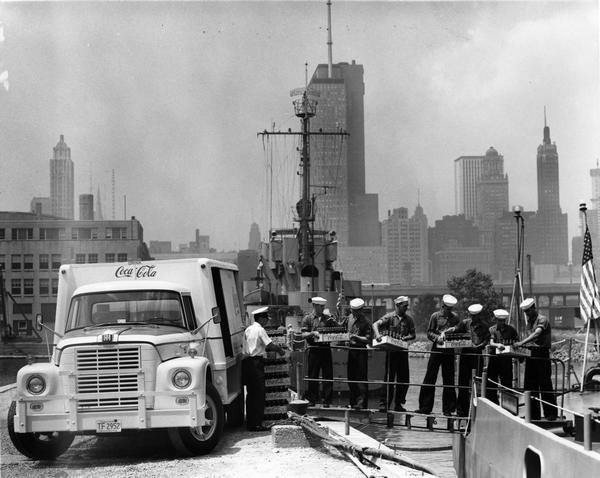 Sailors passing cases of bottled Coca-Cola (soda) from an International truck to a ship docked at Chicago. City skyline in background.