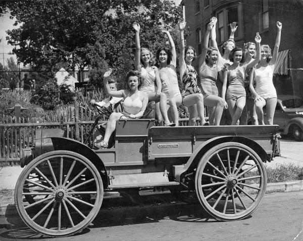 Women in bathing suits sitting on an "antique" International Auto Wagon.