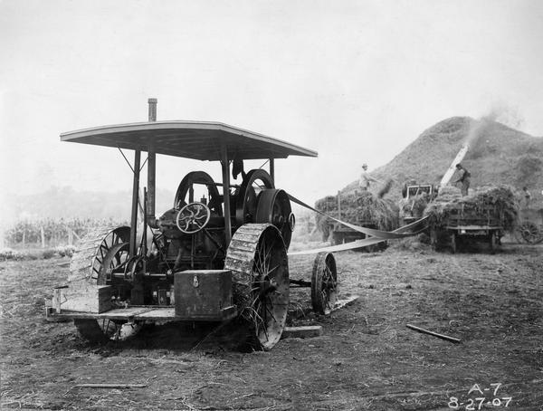 International 20 H.P. Gasoline Traction Engine tractor running a belt-driven thresher on a farm.