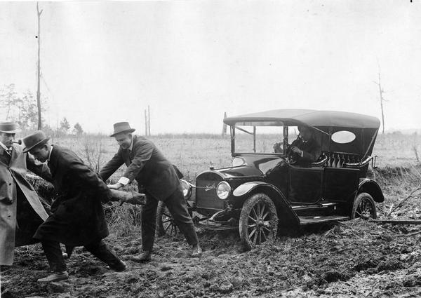 Three men pulling a Maxwell Model 25 touring automobile through a muddy road. Original caption reads: "On the road from Union Springs, and Tuskeegee, Ala., Feb., 1915. Workers [Hudson, Hayne and Hite] in the educational campaign for promoting diversified farming on their travels."