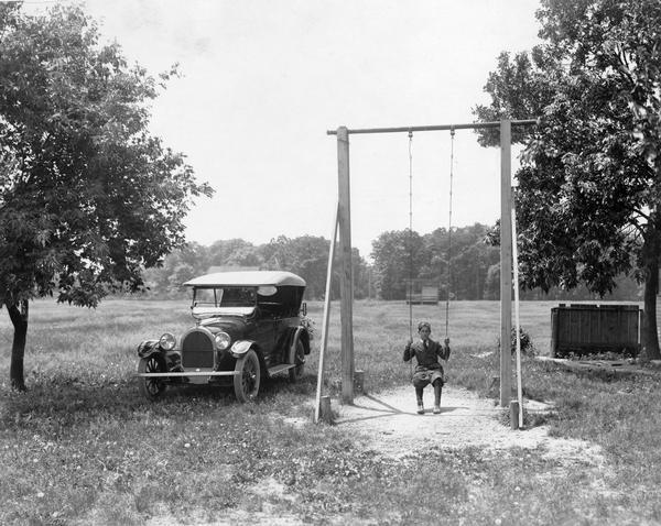 Young boy playing on a school swing. An automobile is parked nearby.
