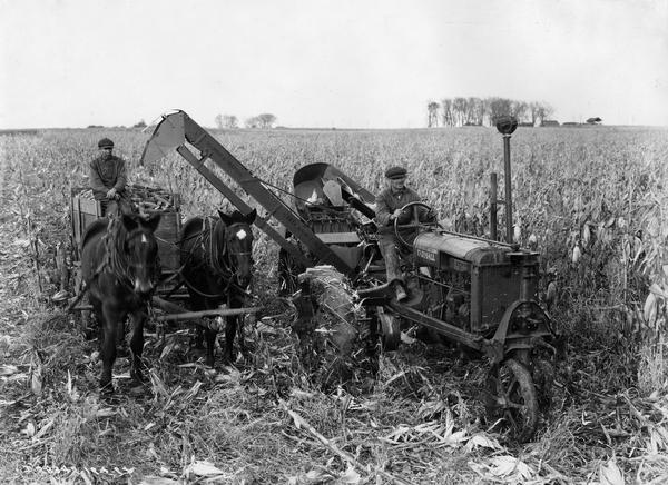 Slightly elevated view of two farmers harvesting corn with a Farmall Regular tractor and a corn picker on the farm of C.M Hick.