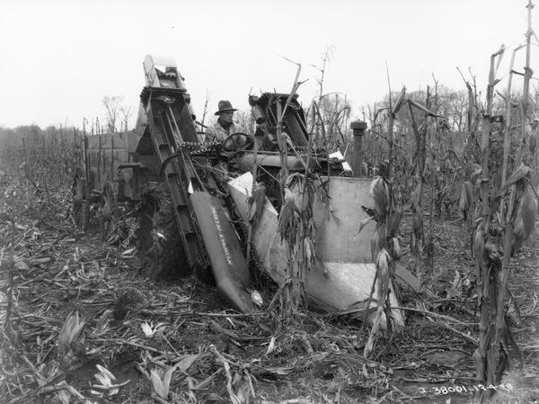 Farmer harvesting corn with a McCormick-Deering two-row corn picker attached to a Farmall Regular tractor. The farmer is smoking a pipe.