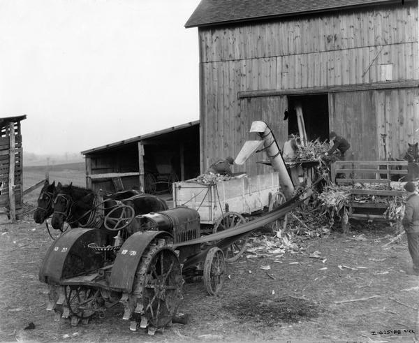 Farmers shredding corn with a McCormick-Deering belt-driven four-roll shredder run by a 10-20 tractor. Behind the tractor and on the right are horse-drawn wagons. Original caption reads: "John Bershinski, Chesterton, Indiana, went out with his McCormick-Deering four-roll corn shredder on the 30th of October and was still shredding corn for the neighbors in January. A few days only he was off because of bad weather conditions. 'The beauty about this shredder is that the fodder never gets too dry for it,' said Mr. Berschinski. 'In fact, the drier the fodder is the better it does the job. That's one reason why I am getting all I can do with it, and more.' The picture was taken on the farm of one of the customers. The old 10-20 for power he thinks is about 13-years-old. 'It runs as well as ever for this belt work,' he said. 'There seems to be no wear-out to it.'"