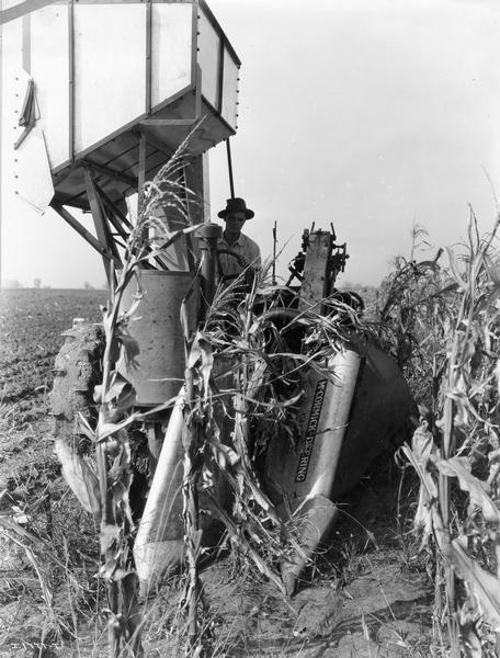 Farmer Adlore Martell operating a McCormick-Deering one row corn picker with overhead grain tank.