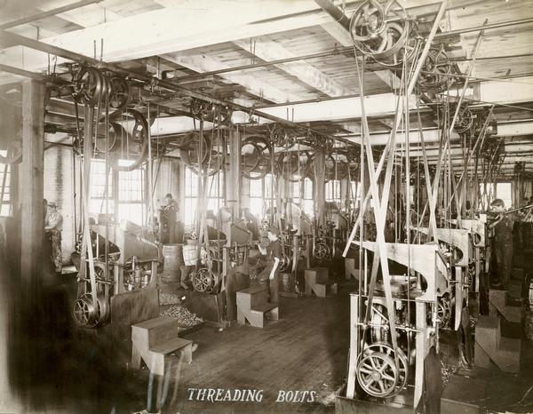 Workers, including some boys, threading bolts with heavy machinery in the Nut and Bolt Department at the McCormick Reaper Works. The factory was owned by the McCormick Harvesting Machine company before 1902. In 1902 it became the McCormick Works of the International Harvester Company. The factory was located at Blue Island and Western Avenues in the Chicago subdivision called "Canalport." It was closed in 1961.