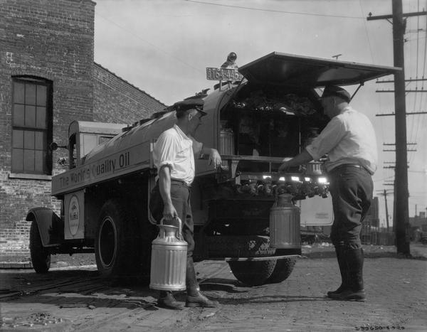 Two men filling oil canisters from the rear of an International Mobiloil truck.