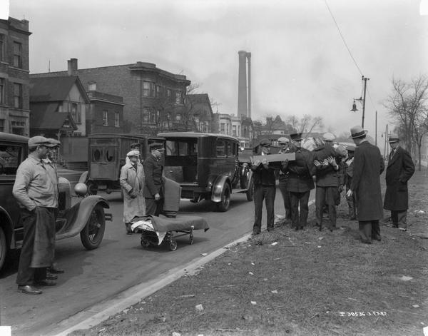Citizens look on as City of Chicago emergency personnel and others carry an injured boy at an accident scene. The event was most likely a staged exercise. An International ambulance owned by the City of Chicago is parked in the background.