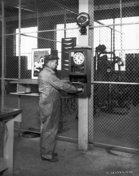 Mechanic punching a ticket at a time clock for a service job at one of International Harvester's motor truck branch service stations. A poster warning of the danger of carbon monoxide is hanging to the worker's left. The man is wearing a jumpsuit with the International "triple diamond" logo.