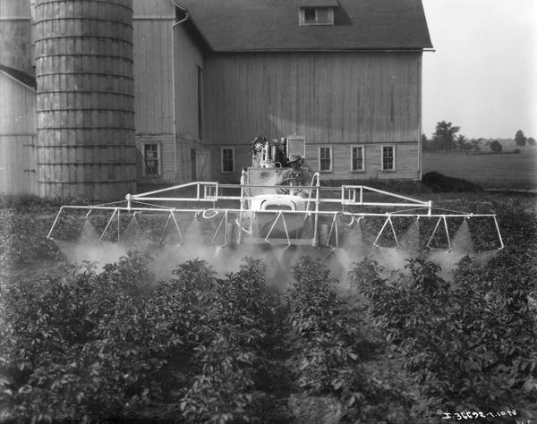 Farmer spraying crops with a modified Chevy automobile with spraying unit.