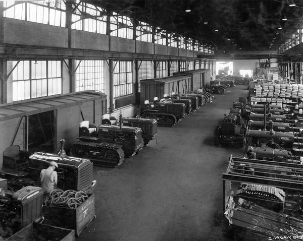 Elevated view of new McCormick-Deering T-40 TracTracTors (crawler tractors) await transfer in the foreign shipping room at International Harvester's Tractor Works. Railroad boxcars are parked along the factory floor.