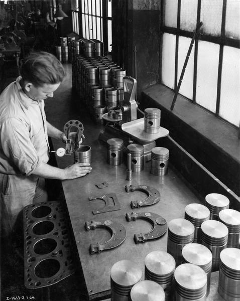 Factory worker inspects tractor pistons at International Harvester's Tractor Works.