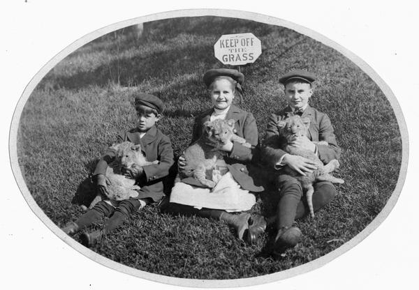 Three children sitting on the ground in front of a "keep off the grass" sign. The children are holding lion(?) cubs. The children may be Cyrus III (1890-1970), Elizabeth (1892-1905) and Gordon (1894-?) McCormick, children of Cyrus Hall McCormick, Jr. (1859-1936).