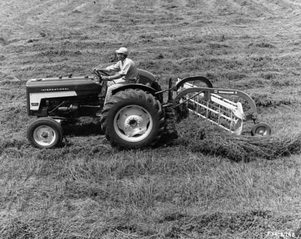 Press release photograph of a man pulling the newly introduced no. 9 side-delivery rake with an International 424 tractor. Original caption reads: "The no. 9 is an economy-priced, fully-mounted, three-point rake for tractors equipped with category I or category II hitches. It rakes a 7-foot swath with a 25 degree basket angle, that saves more leaves and produces more nutritious hay. Coil-spring teeth are regular equipment, rubber-mounted teeth are optional."