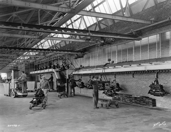 Factory workers preparing completed International truck engines for shipment at International Harvester's Indianapolis Motor Truck Engine Works. Original caption reads: "A typical scene on the loading dock where the finished engines are removed from the power conveyor and loaded into freight cars or trucks for transportation to International truck plants. The conveyor is a continuous chain traveling from the assembly line, through the engine test room, then through the paint booths, and from there to the loading dock. The engines shown here represent the finished products which began as rough parts for their journey through the machine lines, inspection departments, assembly lines, engine test department, and paint booth and are now ready to be assembled to the truck chassis."