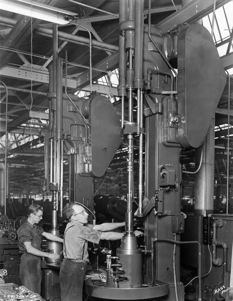 Two machine operators honing truck engine connecting rods at International Harvester's Indianapolis Motor Truck Engine Works. Original caption reads: "Two Barnes honing machines used for honing the crank bearing end of the connecting rod and cap assembly. Note the holding fixtures for honing four connecting rods at one time."
