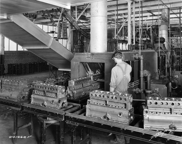 Factory operator washing motor truck engine blocks at International Harvester's Indianapolis Motor Truck Works. Original caption reads: "A Blakeslee washing machine for washing cylinder blocks after all machining operations have been completed. Note the section of overhead conveyor in the background which carries finished parts to the assembly line."