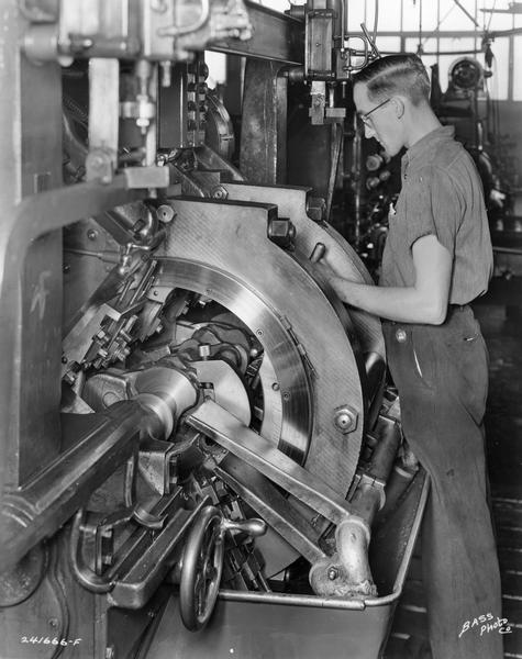 Factory worker using a lathe at International Harvester's Indianapolis Truck Engine Works. Original caption reads: "LeBlond crankshaft lathe showing detail of tool set-up for turning and facing all main bearings simultaneously as well as all diameters on the flange end and pulley end of crankshaft. This sturdy machine makes it possible to grind main bearings to size directly from this turning operation."