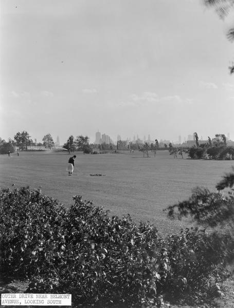 Woman playing golf at Sydney R. Marovitz(?) golf course near Belmont Avenue. The Chicago skyline is in the background.