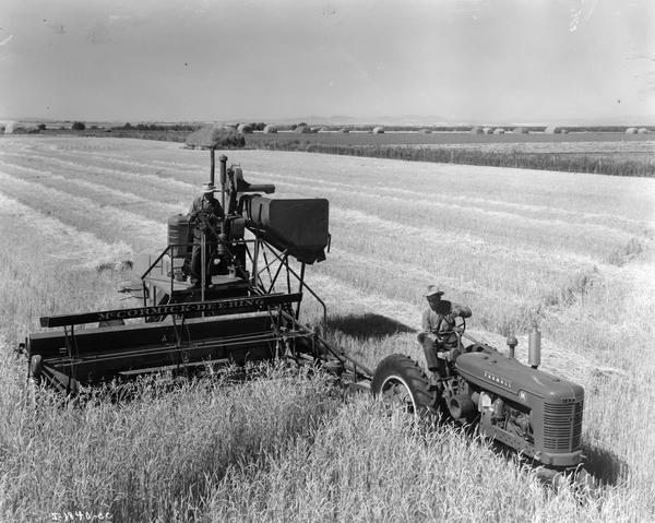 Elevated view of men field testing an experimental McCormick-Deering 12 foot combine with a Farmall M tractor.