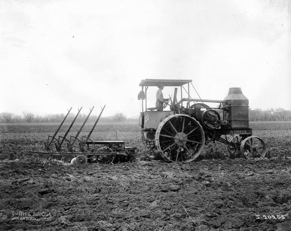 Man pulling a P&O gang plow in a field with a Rumely Oil Pull tractor. The photograph was taken by Smith's Studio for International Harvester.