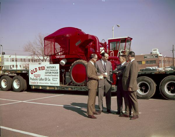 "Old Red," the "first commercial cotton picker," and a new International 622 cotton picker en route to the Smithsonian Institution in Washington, D.C. "Old Red" was donated to the National Museum by Producers Cotton Oil of Fresno, California. The picker was built by International Harvester in 1943. The cotton pickers are parked on a trailer outside International Harvester's Memphis Works. The men in the photograph are (L to R) Dr. George S. Buck, Jr., director of research, National Cotton Council; Memphis Mayor Henry Loeb; J.W. Wegener, IH Memphis Works manager; and Charles M. Albright, IH supervisor of cotton picker sales. At a press conference in Memphis, Wegener pointed out that 96% of the 1969 U.S. cotton crop was harvested by machines, and Dr. Buck said "the development of the cotton picker was the most important single factor which enabled the American cotton industry to stay alive."