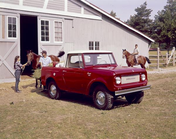 Color advertising photograph of a man unloading bales of hay for horses from the back of an International Scout 4x4 pickup as a girl and boy guide their horses to the truck.
