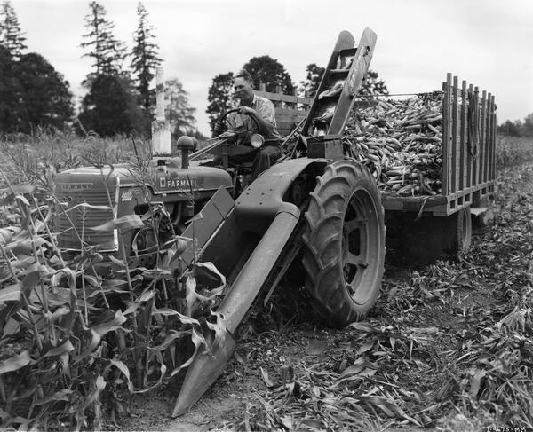 Farmer Dale Eisenman, Jefferson, Oregon, field tests pre-production Model 24-SC corn picker attached to Farmall H tractor on the farm of Douglas Bradley. Caption reads: "This Model 24-SC (sweet corn) picker is approximately the same as the regular No. 24 field corn picker with the husking rolls removed and stripper plates added alongside the snapping rolls. A newly designed star-type snapping roll and high-speed gear case are also utilized."