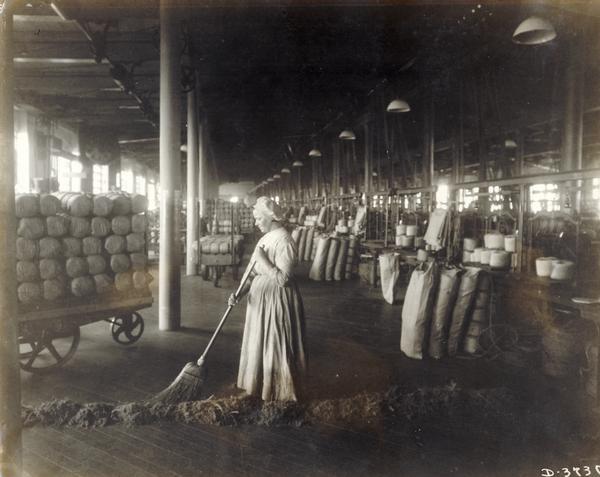 Woman sweeping up debris in a warehouse at International Harvester's Deering Works twine mill. The factory was owned by the Deering Harvester Company until 1902, when it became part of International Harvester Company.