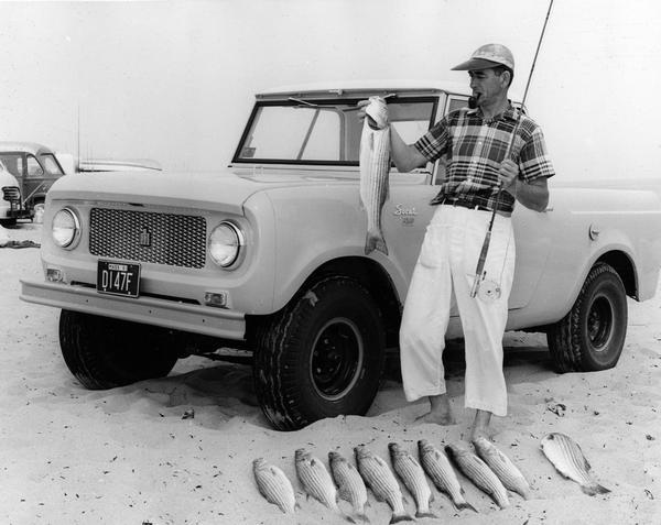 Advertising photograph of a fisherman posing with fish in hand on a beach in front of an International Scout pickup.