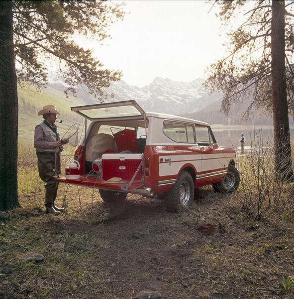 Color advertising photograph of a fisherman unloading gear from the rear of an International Scout II XL pickup near a mountain lake.