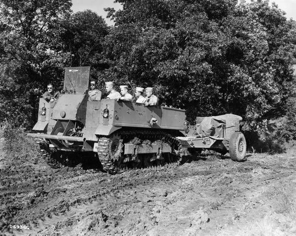 Army personnel pulling a 155mm howitzer with a International M-5 High Speed Prime Mover during a test or demonstration. Original caption reads: "This high speed tractor, a new piece of equipment used by the Army to pull heavy guns, is capable of making speeds up to 35 miles an hour over the roughest type of terrain. It carries a gun crew up to eight men and the driver of the vehicle, as well as a complement of ammunition."