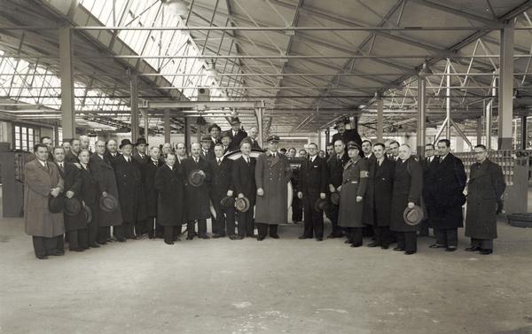 Several men, most likely factory and company managers gathered to celebrate the completion of the first tractor manufactured at International Harvester's Neuss Works in Germany. Two Nazi officials are also with the group.