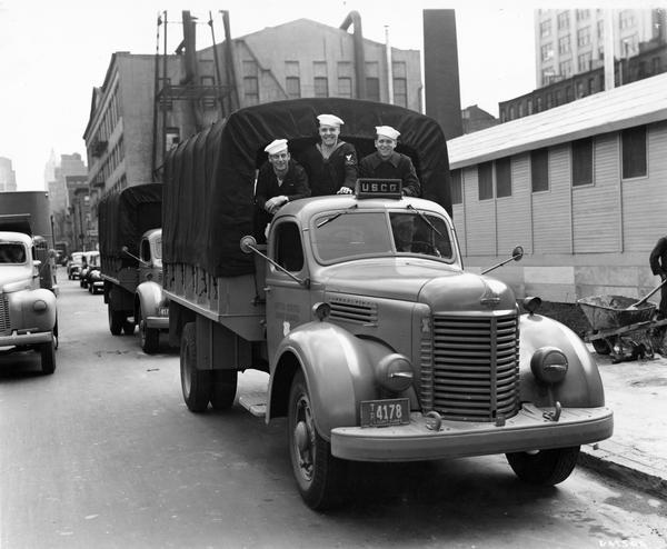 Four members of the U.S. Coast Guard looking out from the back of an International K-6 truck parked on a city street.