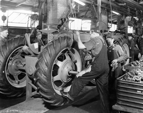Factory workers installing rear wheels and tires on Farmall tractors at International Harvester's Farmall Works.