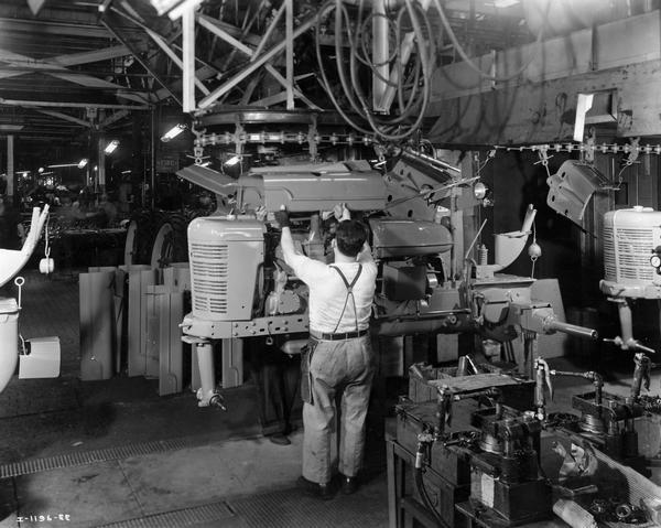 Factory workers on the assembly line at International Harvester's Farmall Works. Original caption reads: "Emerging from the drying ovens after leaving the spray painting booth, the Farmall received its hood."