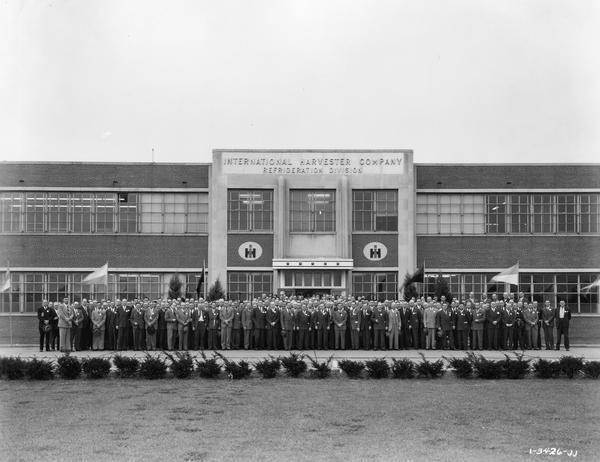 Group portrait of International Harvester's Evansville Works employees wearing suits assembled in front of the factory. The Evansville Works produced refrigerators, freezers and air conditioners.