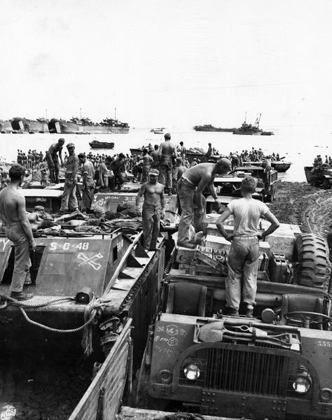 U.S. Marines unloading equipment and vehicles from supply ships at Guam beach. International M-5-H-65 trucks are in the background.