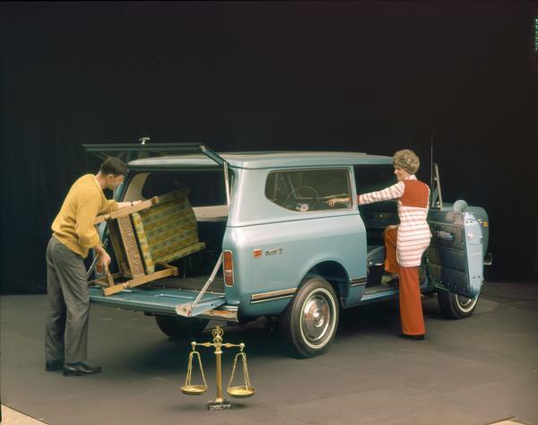 Color advertising photograph of a man loading a chair into the back of a 1972 International Scout II pickup truck as a woman is looking on.