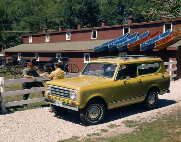 Color advertising photograph of a driver talking with a man in front of a resort building with a number of wagons and canoes in background. A 1972 International Scout II pickup is in the foreground.