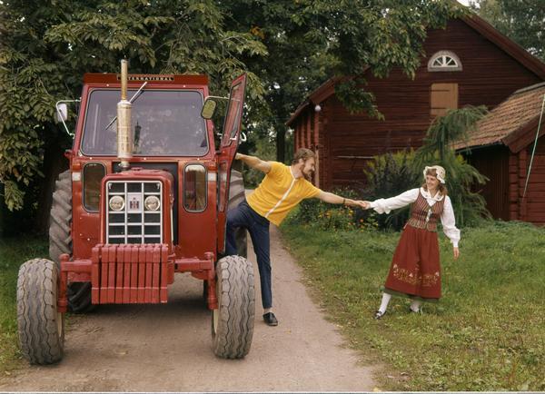 Color advertising photograph of a couple holding hands as the man is preparing to get into an International tractor. The woman is dressed in a Scandinavian costume.