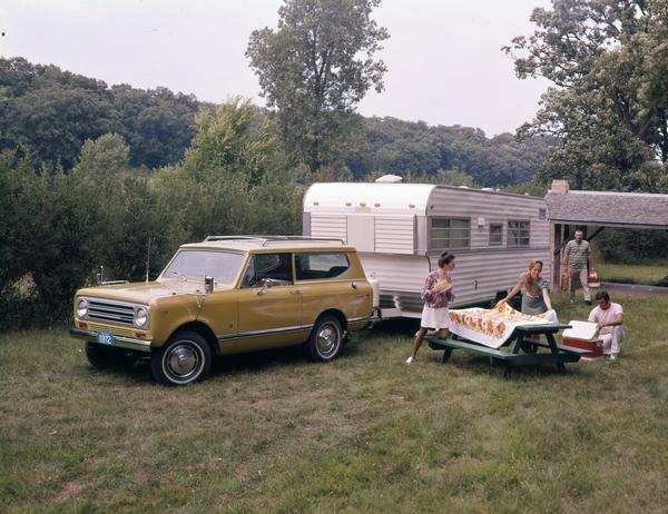 Color advertising photograph of men and women preparing for a picnic at a camp site with an International Scout II pickup and camper parked in the background.
