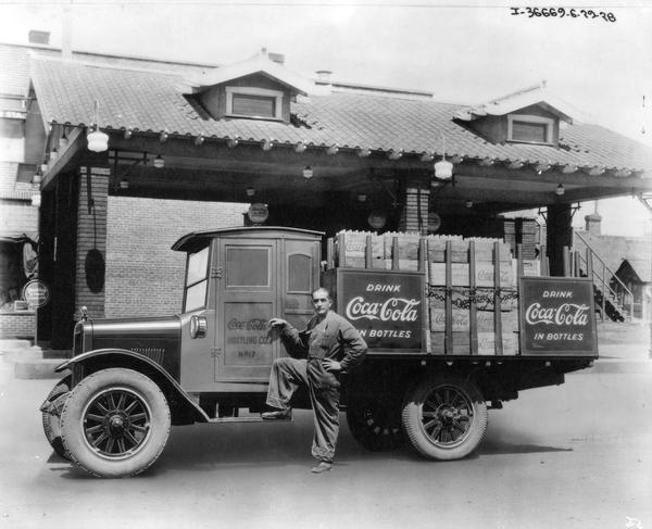 Delivery driver posing with an International Coca-Cola (soda) delivery truck in front of a service station.