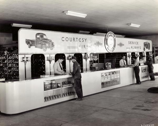 Customers at the parts counter of an International Harvester dealership owned by the Chisholm Brothers of Snake River Valley, Idaho. Behind the counter (left to right) are John F. Chisholm, Donald A. Chisholm, and an unidentified worker.