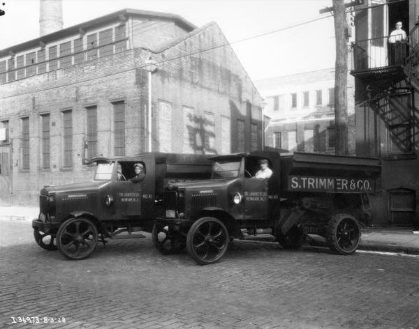 Two International 2 1/2 ton Model 54-C dump trucks parked along a curbside. The trucks were owned by S. Trimmer & Co. International Harvester produced 1,092 54-Cs from 1927 to 1928.