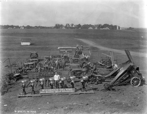 Men standing among McCormick-Deering farm machinery on display in a field. The men are likely from an International Harvester dealership. Machines on display include cream separators, corn binders, grain binders, Farmall tractors, a thresher, a sickle bar mower, a manure spreader, and plows.