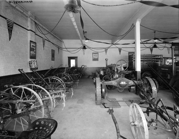 Cultivators, planters, and other McCormick-Deering farm implements in an International Harvester dealership showroom. A truck and a Farmall Regular tractor are on display. The room is decorated with posters, pennants, a literature rack and other advertising.