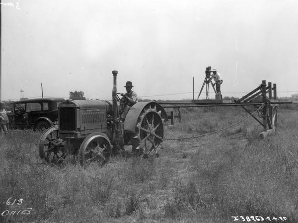 Cameraman riding on a platform pulled by a McCormick-Deering tractor. The man appears to be filming the tractor while it is in motion.
