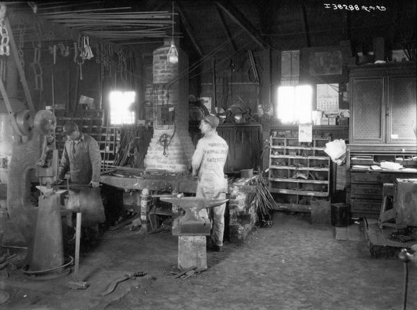 Two blacksmiths at work repairing Farmall tractors in the shop of at the Harvey See Shop in Bates City(?).
